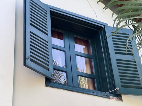 Dark green wooden window shutters are open against a white wall. photo