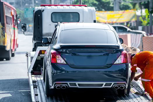 A man in an orange shirt is loading a car onto a tow truck photo