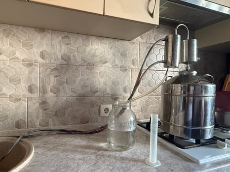 Moonshine still operating on a kitchen stove, producing homemade alcohol. Tubes and a glass jar collecting the distillate, showcasing the art of traditional craft brewing photo