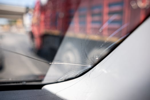 Cracked Windshield Near Busy Roadway With Large Truck in Background During Daylight Hours photo