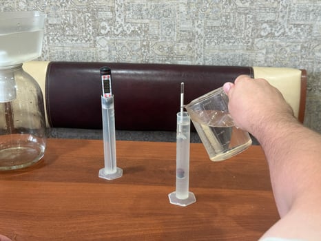 Close up hand of man carefully pouring liquid into graduated cylinder next to digital thermometer and hydrometer preparation of ingredients for crafting homemade alcoholic beverages photo