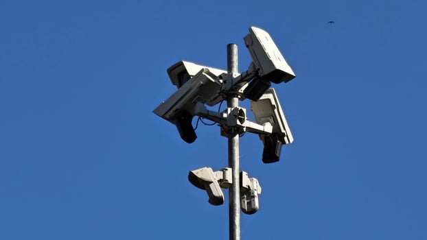 Surveillance cameras are positioned strategically on a tower, set against a bright, clear sky photo