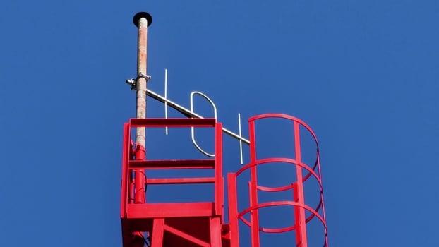 A striking red communication tower stands tall against the brilliant, clear blue sky above photo