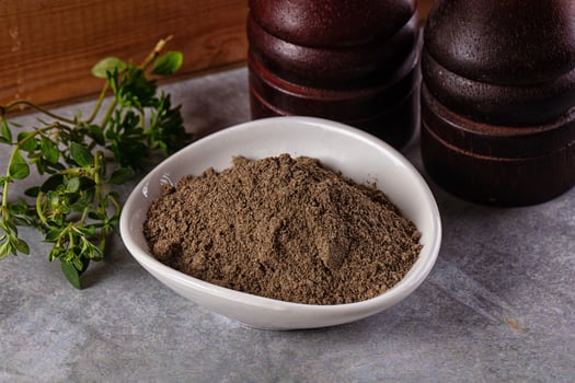 A bowl of brown powder next to a bottle of pepper photo