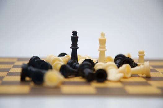 A chessboard displays a dramatic scene of a chess game with numerous fallen pieces surrounding two remaining kings. Two kings, stand apart amidst the chaos, positioned near the center of the image. photo