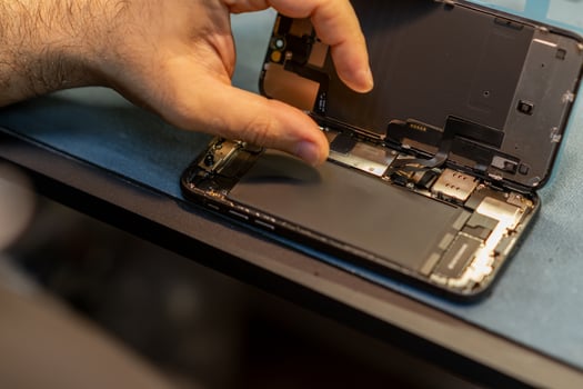Phone Repair Technician Works on a Device With a Disassembled Screen and Internal Components in a Workshop, Focusing on Precision and Detail photo