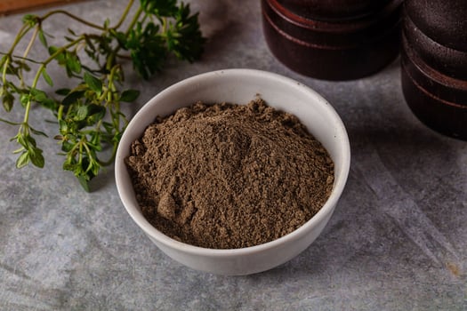A bowl of brown powder next to a knife and a sprig of herbs photo