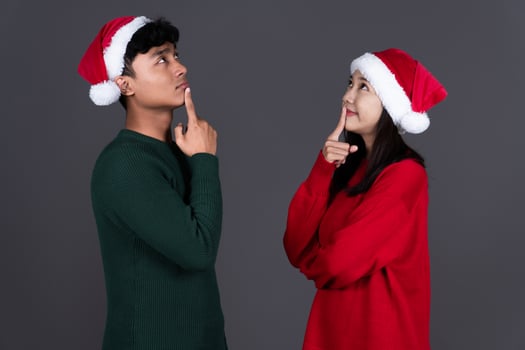 Portrait of Positive Young Asian Couple Thinking Wearing Santa Hat, Christmas Holiday Concept Isolated photo