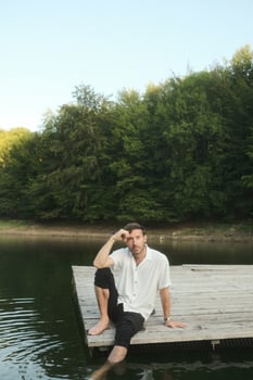 A man is peacefully sitting on a dock overlooking a serene lake photo