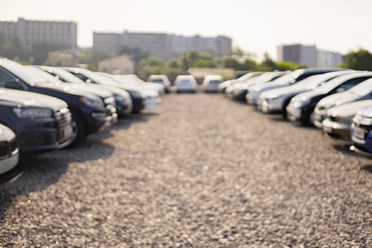 A row of cars is parked outdoors in a gravel lot, with buildings in the background. photo