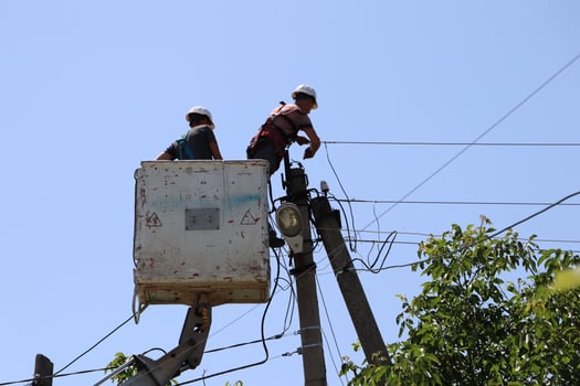 Electricians are diligently working on overhead power lines high above the ground, ensuring photo