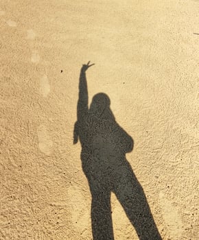 A shadow of a person standing on the beach with their hands up photo