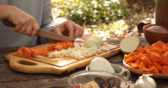 Chopping vegetables outdoors during sunny afternoon, focusing on preparation for healthy meal, featuring carrots, onions, squash, and fresh herbs on wooden cutting board photo