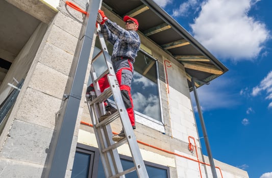 Worker Climbs Ladder to Install Equipment on Construction Site During Sunny Day photo