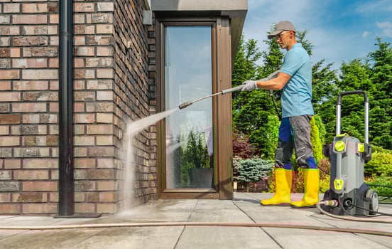 Man Using Pressure Washer to Clean Exterior of Home in Sunny Weather photo