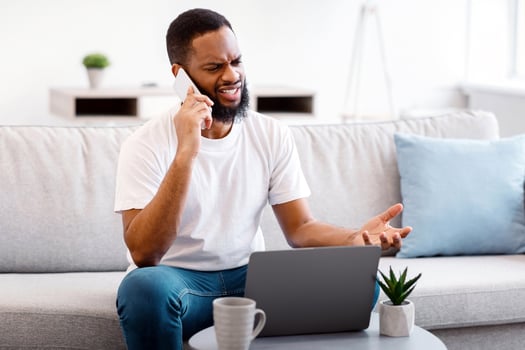 Unpleasant Call. Irritated Black Man Talking On Phone Having Problem With Laptop Or Internet Connection Sitting On Couch At Home. Displeased Customer Calling To Hotline Concept photo