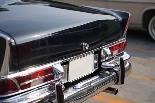 A chrome keyhole above the license plate and a polished rear trunk lock system on a vintage car highlight its sturdy and secure mechanical design.h photo