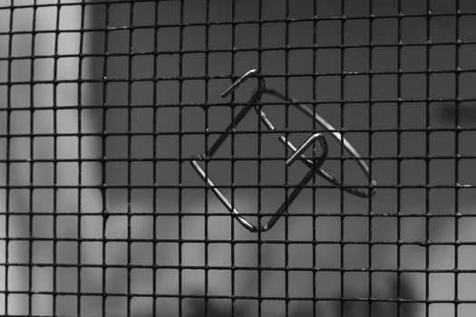 Unraveled wire mesh entraps a delicate paper clip in an abstract interplay of shadow and light during a quiet afternoon photo