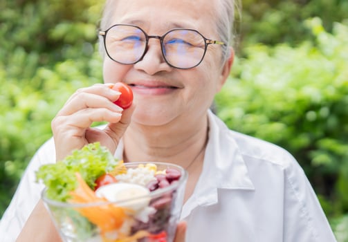 Happy Asian retirement women holding a tomato with fresh salad bowl for good health at outdoor. photo