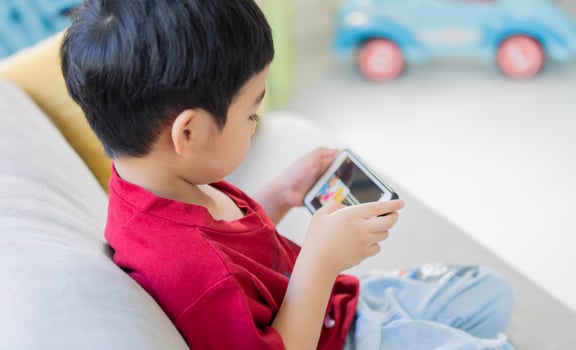 Back view of little cute Asian boy in a red T-shirt playing games on a tablet and watching cartoons. photo