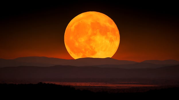 Giant Orange Moon Rises Over Silhouetted Mountain Ranges at Dusk. photo