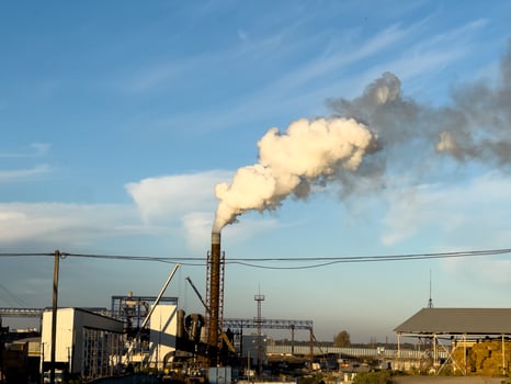 White smoke rises from a tall chimney against a clear blue sky, highlighting industrial activity in an urban environment photo