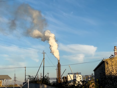 Factory smokestack emits thick clouds of smoke into the bright afternoon sky, highlighting industrial activity and environmental concerns photo