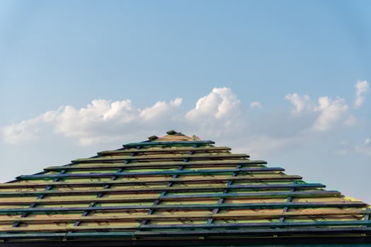 Workers are installing wooden beams on a roof, with a clear blue sky and fluffy clouds above, creating a serene construction setting photo