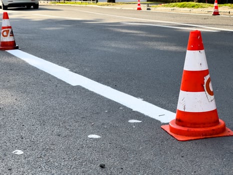 Traffic cones are positioned along a freshly painted lane marking in an urban area during road maintenance work, ensuring safety for drivers photo