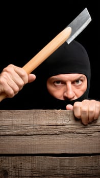 A man in a black mask peeking over a wooden fence with a large knife photo