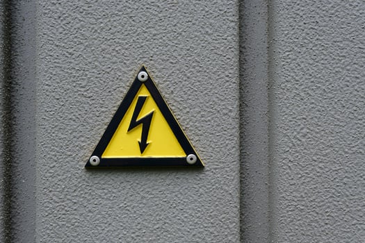 On a grey wall of a Danish transformer house, a 3D warning sign for an electric shock photo
