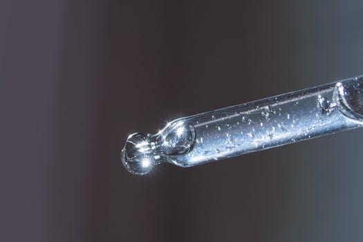Close-up of a glass pipette with liquid droplet reflecting light on a gradient background. photo