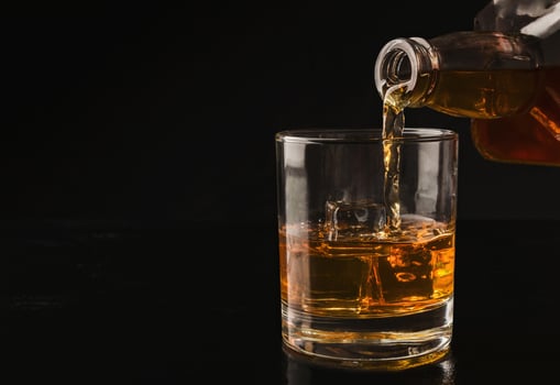 Pouring whiskey from bottle into glass with ice cubes on black background, copy space photo