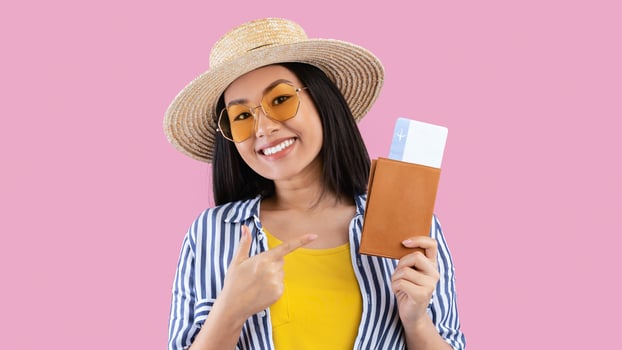 Time For Vacation. Excited Asian Woman Holding And Pointing At Passport And Plane Boarding Pass Tickets, Ready For Summer Trip, Wearing Straw Hat And Sunglasses, Isolated On Pink Studio Wall, Banner photo