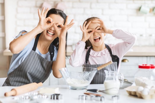 Cute little girl and her beautiful mother are playing and smiling while baking in kitchen at home, freespace photo