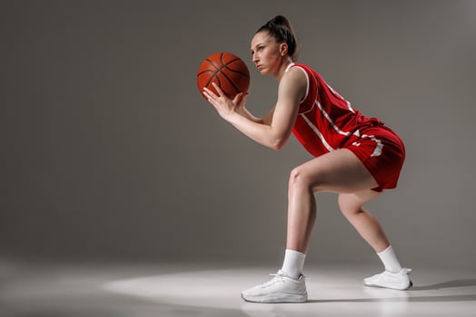 Focused female basketball player in red uniform squatting and preparing to pass the ball, studio action shot photo