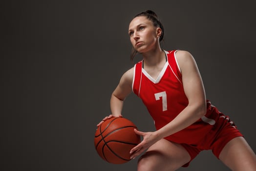 Female basketball player in red uniform dribbling and focused in action, isolated on dark studio background photo