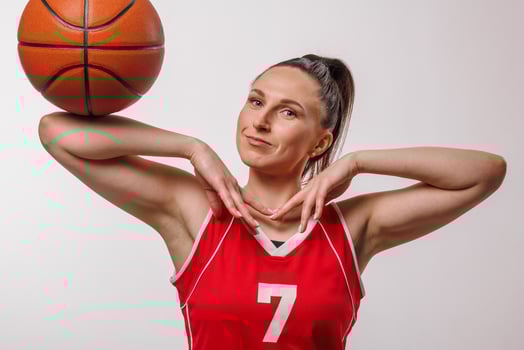 Confident female basketball player in red uniform posing with ball, expressive sporty studio portrait photo