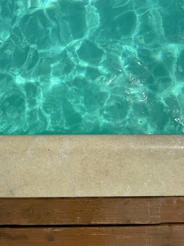 Turquoise water with sunlight shimmer near stone edge and wooden planks evokes sense of summer peace spa lifestyle outdoor wellness and clean aesthetic for travel moodboard and design projects Serene photo
