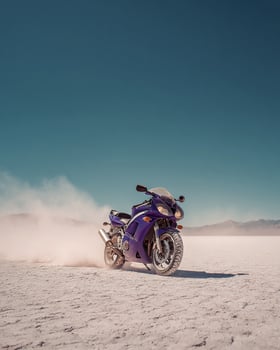 Side View of Racing Purple Motorcycle With Dust Trail Across Salt Plain and Blue Sky in High Speed, Minimal, and Contrasty Frame photo