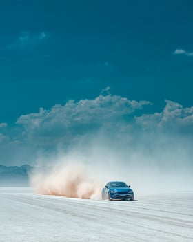 High Speed Blue Supercar Driving Across Vast White Salt Desert with Dust Trail, Contrasting Blue Sky, and Side Profile for Ad and Editorial Use photo