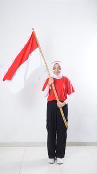 Muslim Asian girl celebrate Indonesia independence day in red and white outfit by holding Indonesian flag isolated on white background photo