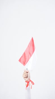 Woman hand with red and white Indonesia flag color attribute holding mini Indonesia flag decoration to celebrate Indonesia independence day celebration isolated on white background photo