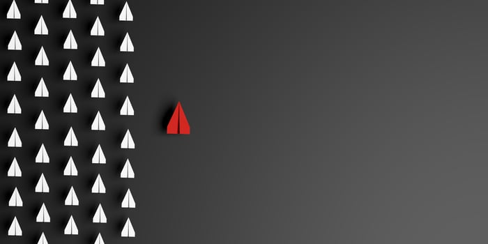 Red paper airplane leads a group of white plains on dark background, symbolizing leadership, innovation, standing out, individuality, unique vision, breaking from conformity, business success. 3d photo