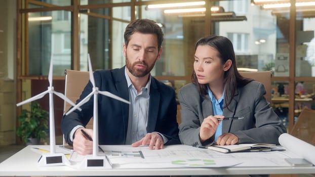 Multinational business team discussing eco project investment wind turbine model sustainable energy Korean businesswoman Caucasian businessman teamwork environment planning innovation green startup photo