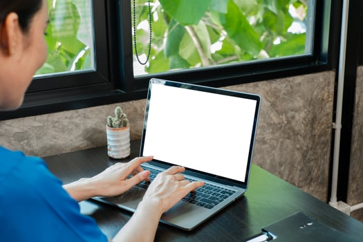 Woman typing on a laptop with a blank screen in a modern office, surrounded by greenery and natural light. photo