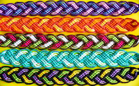 Selective focus of multi-colored woven DIY friendship bracelets Pigtail handmade of embroidery bright thread with knots on yellow background photo