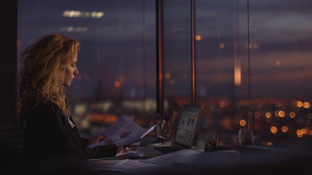 Businesswoman Reviewing Documents at Night with City Lights in Background from High-Rise Office Window photo