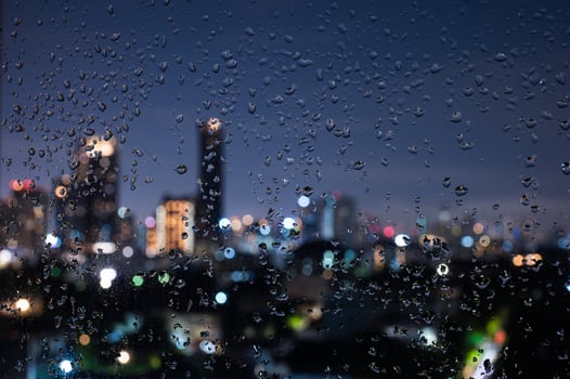 Rain drops on glass window in monsoon season with bokeh of city lights and buildings background. photo