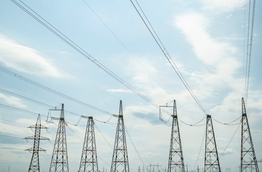 Row of high voltage power lines and transmission towers under a bright cloudy sky. photo